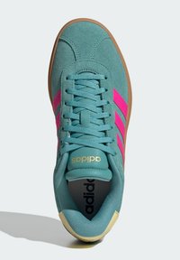 Teal mockasiner i mocka med rosa tre ränder, brun gummisula och guldlogotyp på tungan. Har en vadderad krage och mesh-foder.