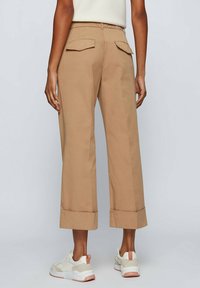 Beige cropped broeken met grote achterzakken en opgerolde boorden. Gemaakt van een lichte stof, hebben ze een rechte pijp.