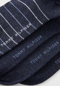 Calze di un blu scuro con strisce verticali bianche e il logo "TOMMY HILFIGER" in azzurro. Il tessuto appare liscio e morbido.