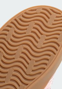 Sole of a pink sneaker featuring a textured, wavy pattern and a gum rubber material, designed for grip and durability.