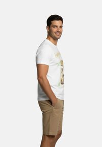 Camiseta de algodón blanca con un estampado gráfico, combinada con pantalones cortos beige. La camiseta tiene un escote redondo y mangas cortas.