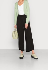 Vihreä ylisuurikokoinen neuletakki, valkoinen toppi, mustat leveälahkeiset housut ja vaaleanvihreä käsilaukku. Paksupohjaiset loaferit mustalla pohjalla viimeistelevät asun.