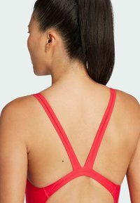 Red athletic swimsuit featuring thin straps with a crossed back design. Made from smooth, stretchy material with a minimalist look.
