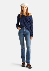 Top de manga larga con hombros al descubierto en color azul marino, combinado con jeans azul medio de tiro medio y mocasines marrones. La modelo lleva un boina de fieltro blanca. Diseño simple, ajuste casual.
