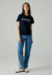 T-shirt de algodão azul-marinho com o logótipo "Red Bull RACING" em branco. Combinado com jeans azul-claro e ténis brancos. Design simples e casual.