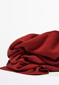 Couverture en tricot rouge, à la texture douce, superposée et drapée, avec un bord en côtes sur un côté, dans une couleur chaude et riche.