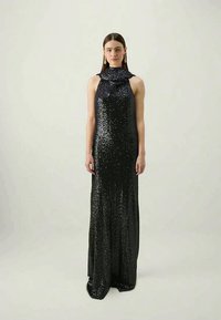 Melnas sekvīru vakartērps ar augstu apkakli un plūstošu, taisnu siluetu. Iezīmējas ar salocītu apkakles detaļu un gludu tekstūru.