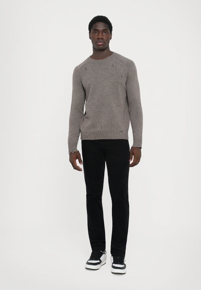 Pull en tricot marron avec un col rond, des poignets et un ourlet côtelés ; associé à un pantalon slim noir et des baskets noir et blanc.