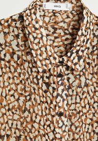 Chemise à imprimé léopard dans des nuances de marron, crème et noir. Tissu léger avec un col à revers et des boutons à l'avant.