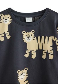 Mustapaita, jossa on leikkisiä vaaleanbeigejä tiikerikuvastoja. Pyöreä pääntie ja pehmeä, teksturoitu kangas. Tiikereiden asennot vaihtelevat kankaan pinnalla.