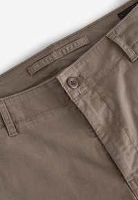 Khaki cotton pants with a ribbed texture, featuring a button closure and belt loops, seen from above focusing on the waistband.