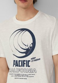 Katoenen T-shirt in lichtcreme, met een donkerblauwe afbeelding van golven en een skateboarder. Tekst bevat "PACIFIC CALIFORNIA" en verschillende details van golven.