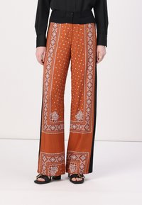 Vide benbukser i oransje med hvit paisley og intrikate mønstre. Svart sidepaneler, laget av lett materiale, med en glatt tekstur.