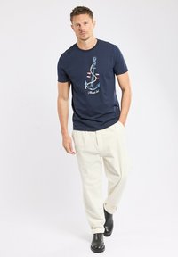 T-shirt bleu marine avec un graphique d'ancre en bleu clair et des accents rouges, associée à un pantalon en velours côtelé crème et des bottines noires.