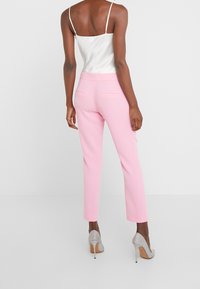 Rosa skräddarsydda byxor med smal passform, slät textur och bakfickor, i kombination med en vit linne och silverskor med hög klack.