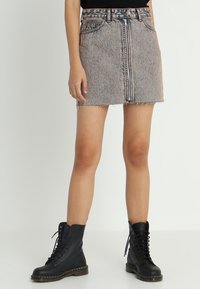 Minifalda de denim con textura desgastada, cierre de cremallera frontal y dobladillo deshilachado. Combinada con botas negras de tobillo con cordones.