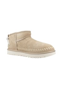 Stivaletto alla caviglia in suede beige con una texture morbida, dettagli di cuciture bianche lungo la cucitura e una suola in gomma leggera. Presenta una linguetta laterale per facilitarne l'indossamento.