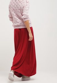 Gonna lunga rossa con un design fluido, abbinata a un maglione lavorato a maglia rosa chiaro con un motivo testurizzato. Completata con calzature casual.