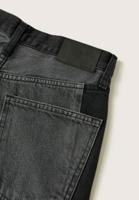 Vue arrière d'un jean en denim bicolore noir et gris foncé avec poche arrière visible et patch de marque en cuir noir.