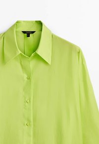 Chemise boutonnée vert clair avec un col pointu, trois boutons visibles et une texture de tissu lisse.