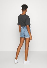 Shorts en denim bleu avec une taille froncée, associés à un t-shirt gris. La tenue est complétée par des baskets blanches.