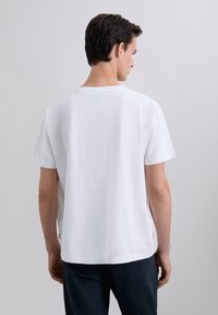 Camiseta de algodón blanca con mangas cortas, corte cuadrado y escote clásico. Textura suave; sin patrones ni gráficos visibles.