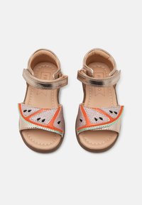 Sandalias de tiras metálicas doradas con un diseño de sandía que presenta tonos de rosa, naranja y verde. Textura suave y suelas planas.
