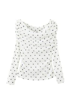 Blouse blanche à manches longues à pois noirs avec un col drapé asymétrique sur un fond uni.