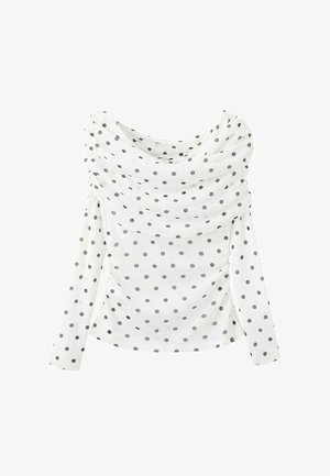 Blouse blanche à manches longues à pois noirs avec un col drapé asymétrique sur un fond uni.