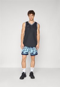 Black sleeveless basketball jersey with white accents, paired with light blue shorts featuring abstract patterns, and black athletic shoes.