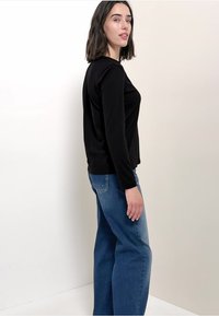 Svart långärmad topp med rund halsringning, kombinerad med ljusblå vida jeans. Enkel design, slät textur och klassisk passform.