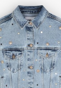 Giacca di jeans blu chiaro con tasche a patta, decorata con borchie metalliche, perle e bottoni decorativi. Presenta un colletto classico e chiusura con bottoni.