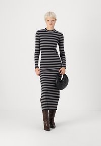 Vestuário listrado de mangas longas em tecido canelado preto e cinza, com silhueta ajustada, fenda lateral, combinado com uma bolsa redonda preta e botas castanhas.