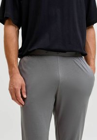 Pantaloni sportivi grigi con una finitura morbida e vita elastica, abbinati a una t-shirt nera dal taglio morbido. Texture orizzontale visibile sui pantaloni.