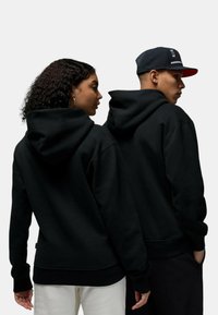 Felpe nere con cappuci grandi e polsini a costine. Il tessuto sembra morbido; la vista dal retro mostra un design pulito con dettagli minimi.