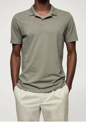 Polówka w kolorze oliwkowej zieleni z krótkim rękawem, wykonana z oddychającej tkaniny, z klasycznym kołnierzykiem i luźnym krojem. Zestawiona z jasnobeżowymi spodniami.