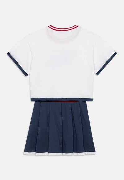 Ensemble deux pièces en coton comprenant un haut court blanc avec des accents rouges et bleu marine, et une jupe plissée bleu marine avec un ourlet blanc.