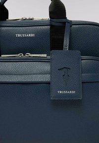 Námořnická modrá kožená taška na notebook s texturovaným povrchem, dvojitými zipy, nastavitelnými popruhy a odpovídající visačkou na zavazadla s vylisovaným logem.