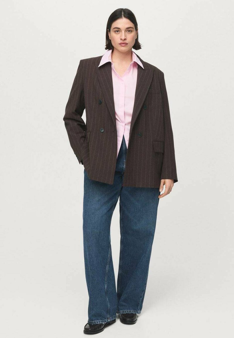 Blazer marrón de doble botonadura con raya diplomática, camisa rosa claro debajo, vaqueros azules de corte holgado y zapatos negros. Tela suave y diseño estructurado.