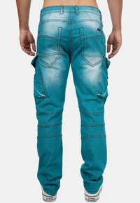 Pantalons cargo turquoise à coupe slim, dotés de poches latérales, de surpiqûres contrastantes et d'une texture délavée. Finition avec une taille et des passants de ceinture.