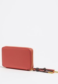 Cartera rectangular con cremallera en piel lisa de color rojo-anaranjado. Presenta una cremallera dorada y cuerdas con textura en negro y rojo con puntas de metal.