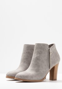 Botines de ante sintético gris con punta redondeada, cremallera lateral y tacón medio en bloque con rayas verticales. Textura suave, diseño minimalista.