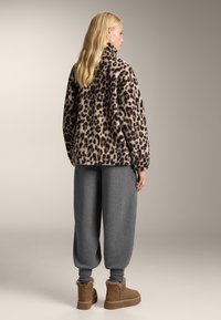 Giacca oversize con stampa leopardata in pelliccia sintetica, abbinata a pantaloni della tuta grigi e stivaletti alla caviglia color cammello. Texture morbida, colletto alto, vestibilità comoda.
