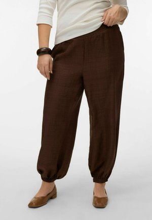 Pantalones de ajuste holgado de color marrón oscuro con textura, puños elásticos, combinados con zapatos bajos color canela y una camiseta blanca de manga larga.