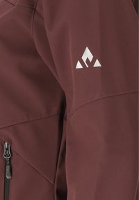 Maroon jacket sleeve with a white geometric logo near the shoulder and a black zipper on a side pocket in view.