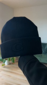 Black knitted beanie with a ribbed texture and a folded cuff. Features a tonal logo on the front for subtle branding.