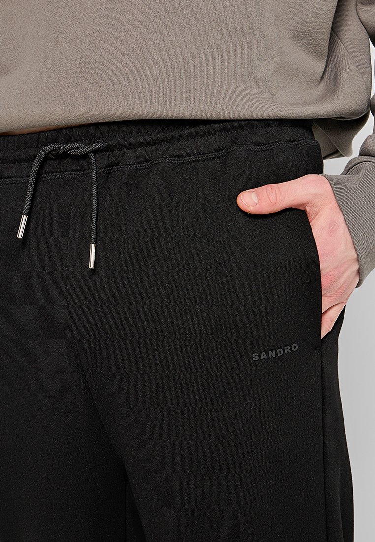 Svarta joggerbyxor med elastisk midja, justerbar dragsko och sidoficka. Tyget har en slät yta; logotypen visas på låret.