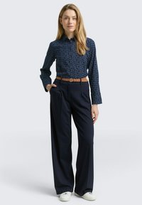 Marineblauw met patroon, overhemd met lange mouwen en kraag, gecombineerd met hooggeplaatste, wijde marineblauwe broek en witte sneakers.