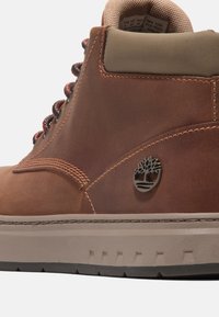 Braune Lederstiefel mit hellen Akzenten, runden Schnürsenkeln und einem gepolsterten Kragen. Mit einem Metall-Logo und einer strukturierten Gummisohle.