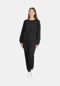 Schwarzes Sweatshirt- und Hosenset mit strukturierter Optik. Das Material wirkt weich und lässig. Weiße Sneakers vervollständigen das Outfit.